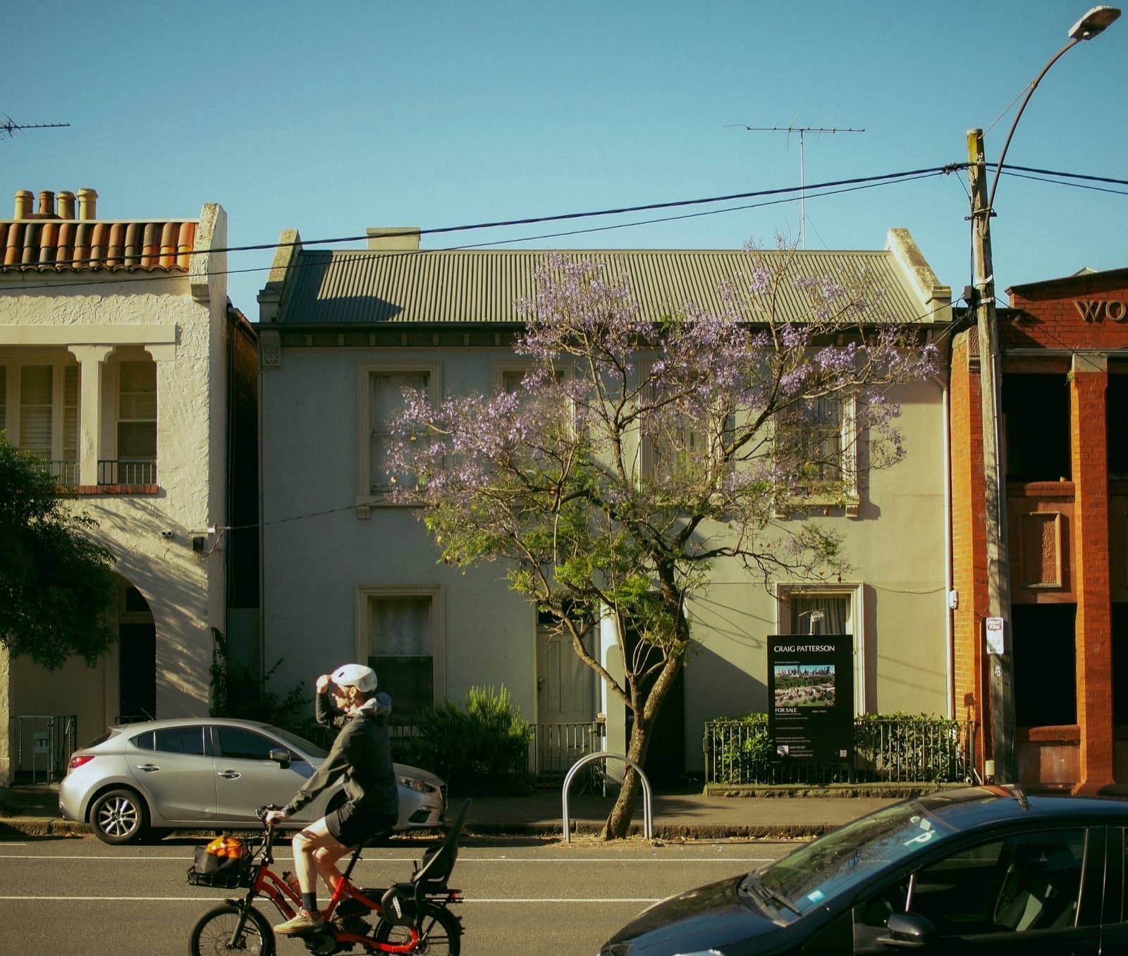 Melbourne terrace houses with a for-sale board under a jacaranda